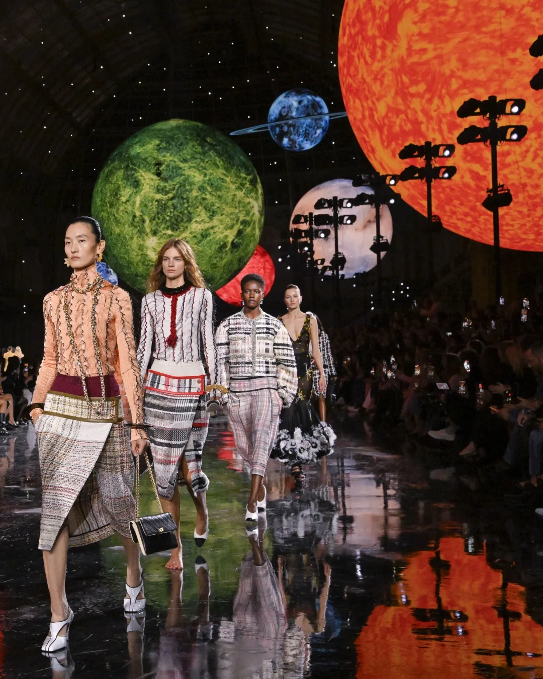 Models walk the space-themed runway for the Chanel Spring Summer 2026 fashion show in a set designed with huge, glowing planets and a starry sky. 
