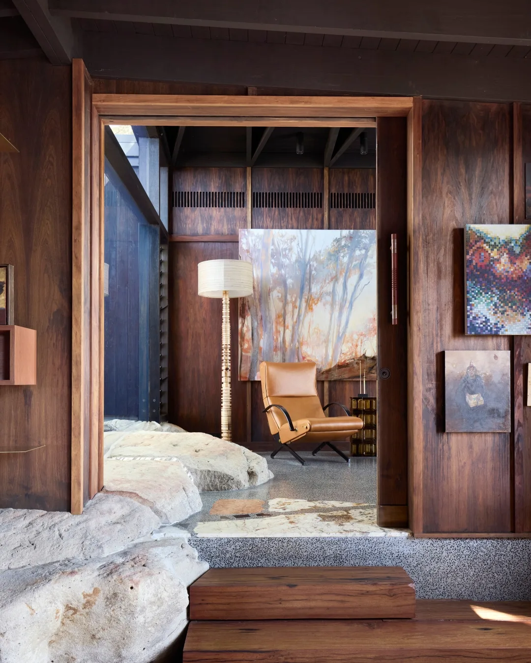 Interior with wooden walls, large rocks, leather chair, floor lamp, and artwork. 