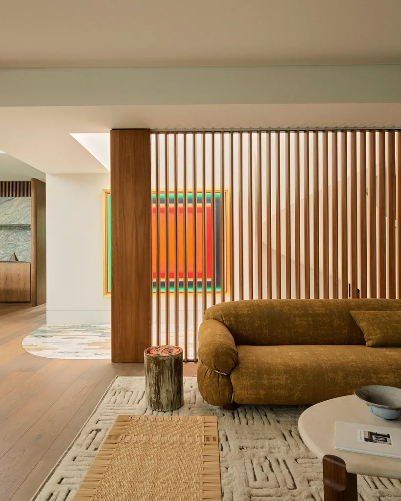 Modern living room with a textured brown sofa, wooden accents, abstract art, and a round coffee table on a patterned rug.