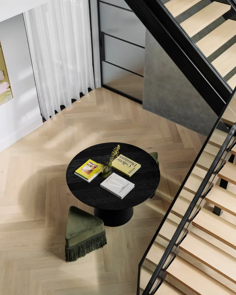 A bird's eye view of a living area with herringbone engineered timber flooring, a black round dining table and green velvet tasseled stool.