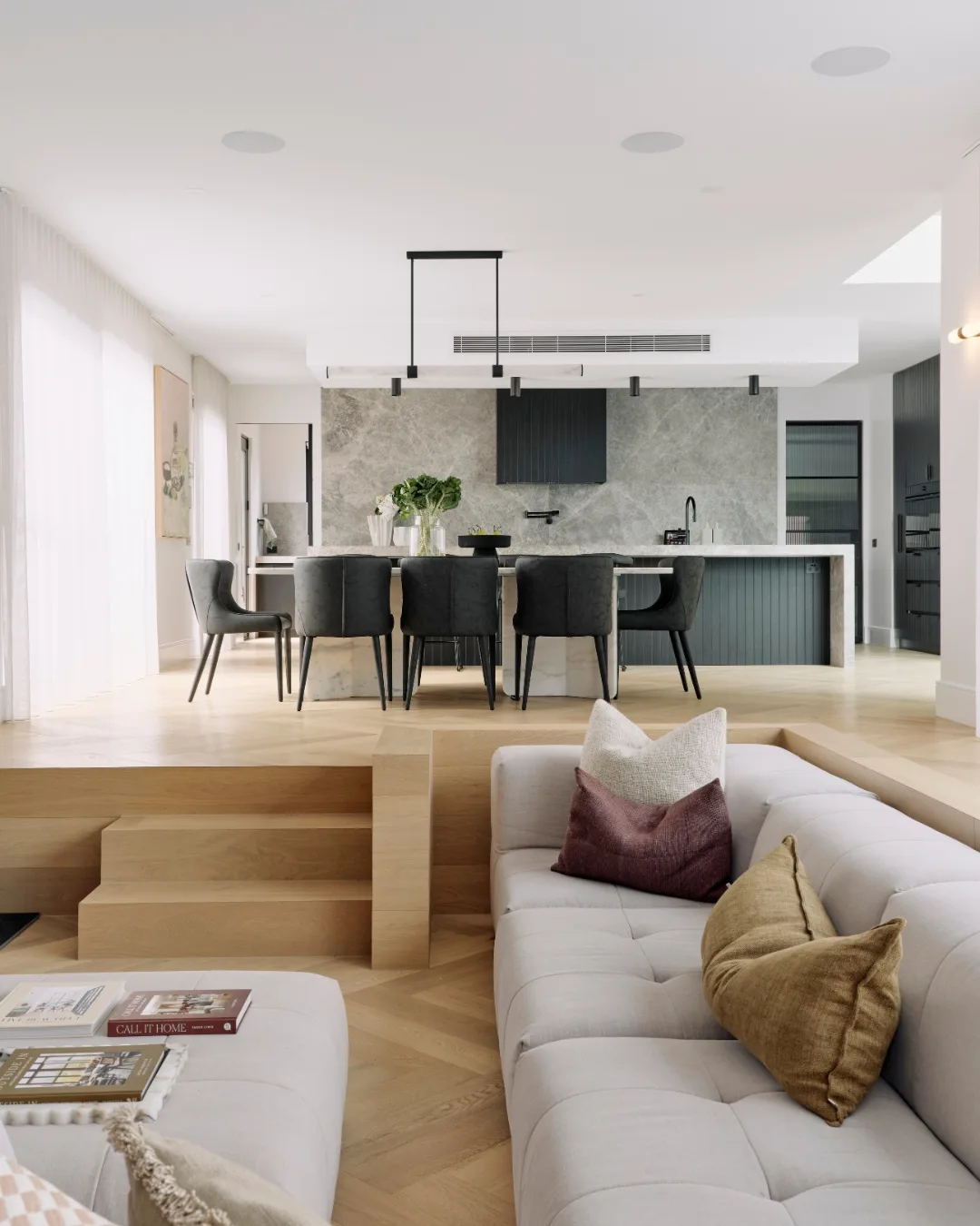 A sunken living room with engineered timber flooring stairs leading up to an open kitchen and dining area. 