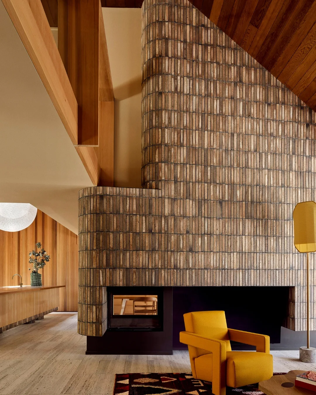 Modern interior with a large, textured brick fireplace, a yellow armchair, and wood accents. 