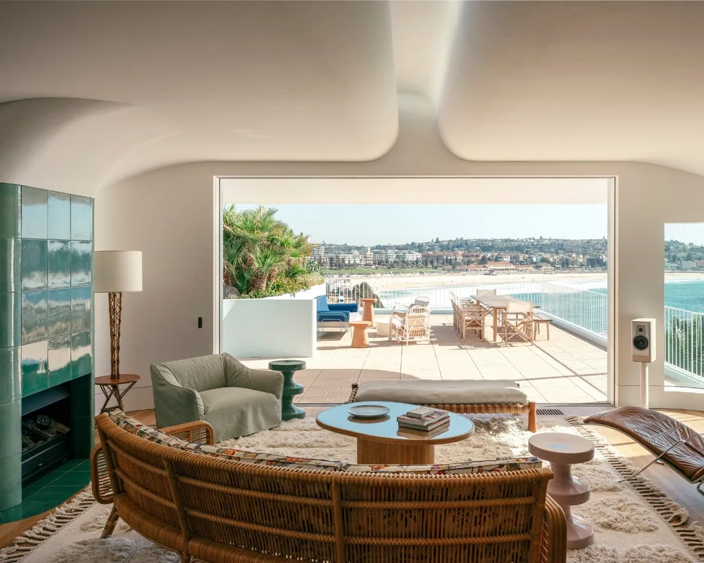 Coastal living room with beach view, rattan sofa, retro green tiled fireplace and abundance of natural light.