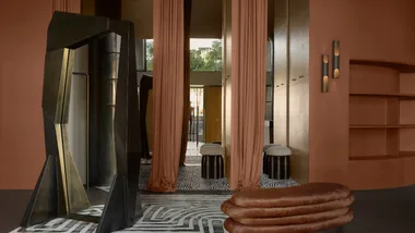 Modern interior with geometric mirror, peach curtains, textured stools, and patterned carpet.