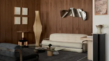 A wooden panelled room with white boucle couch, paper floor lantern and abstract metallic artwork hanging on the wall.