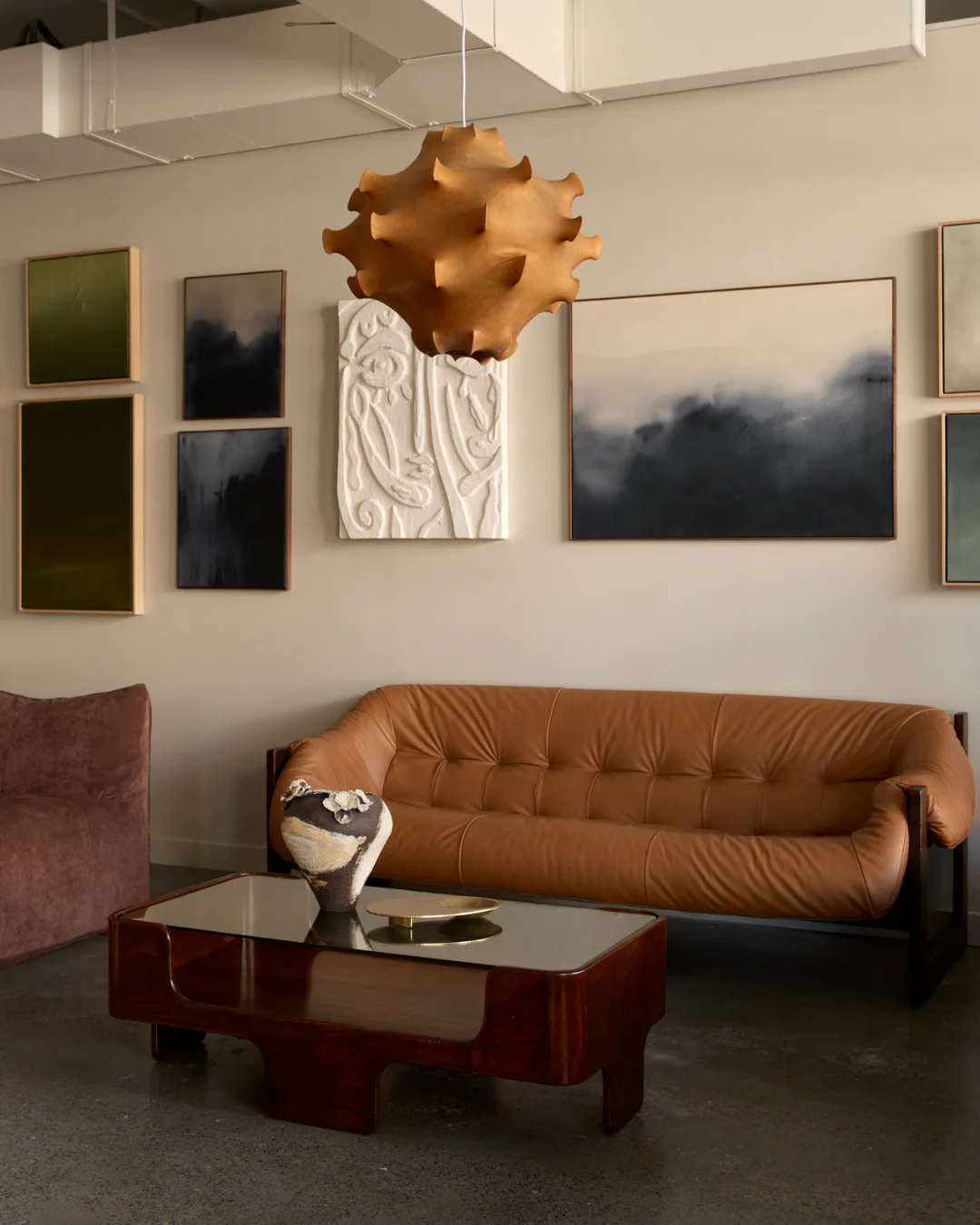 Leather couch with beige abstract lantern, tortoise shell coffee table, ceramic vase and contemporary, monochromatic artwork in wooden frames.