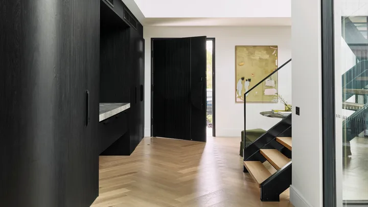 Engineered Timber Flooring laid in a herringbone pattern in the hallway of a modern home with black timber cabinetry and a black timber clad front door leading out to the street.