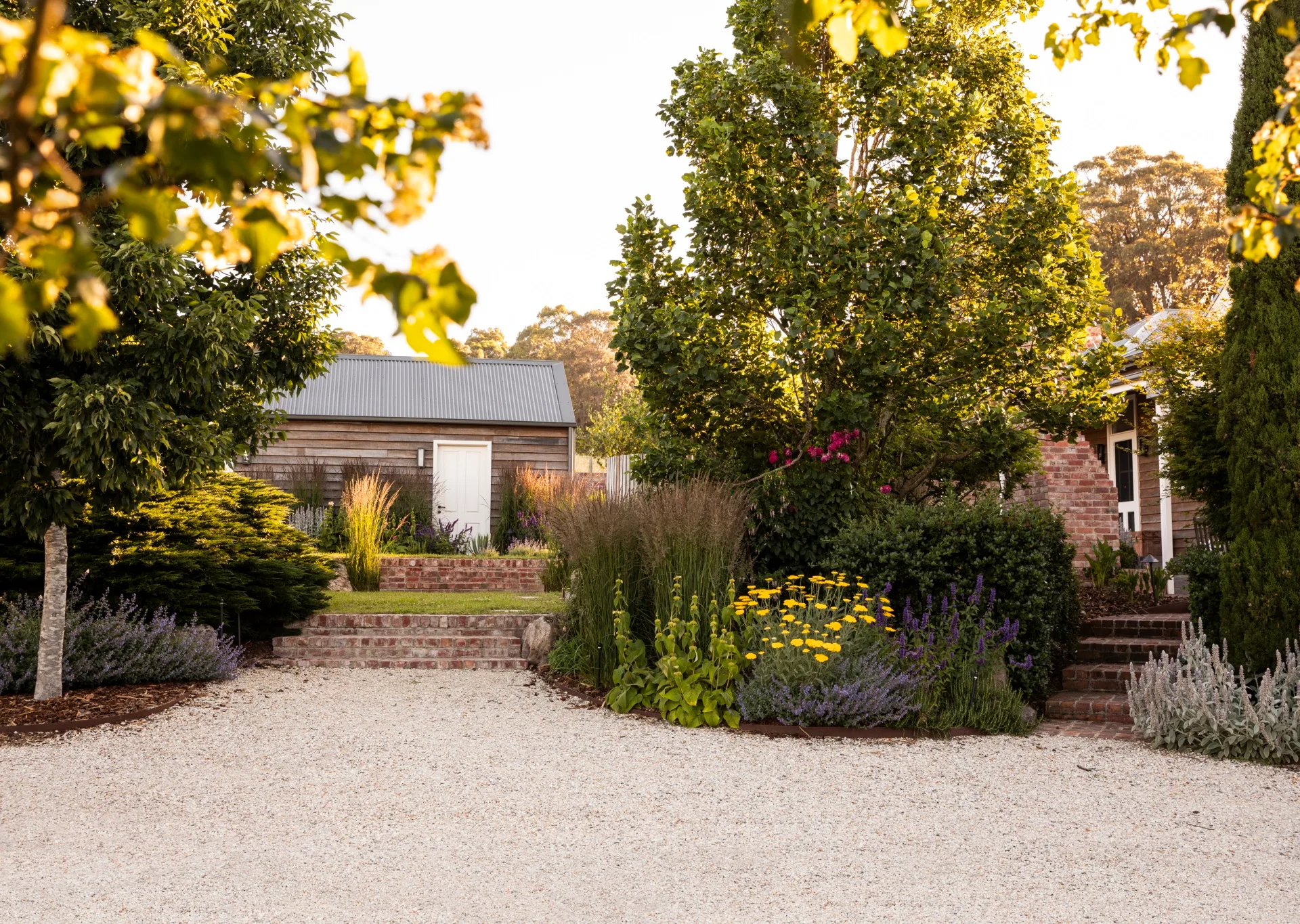 A large gravel area with colourful plantings and mature trees