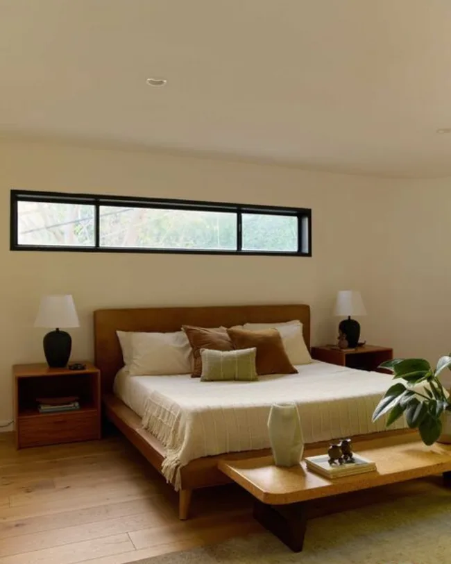 a bedroom with neutral palette, palnts and timber footstool