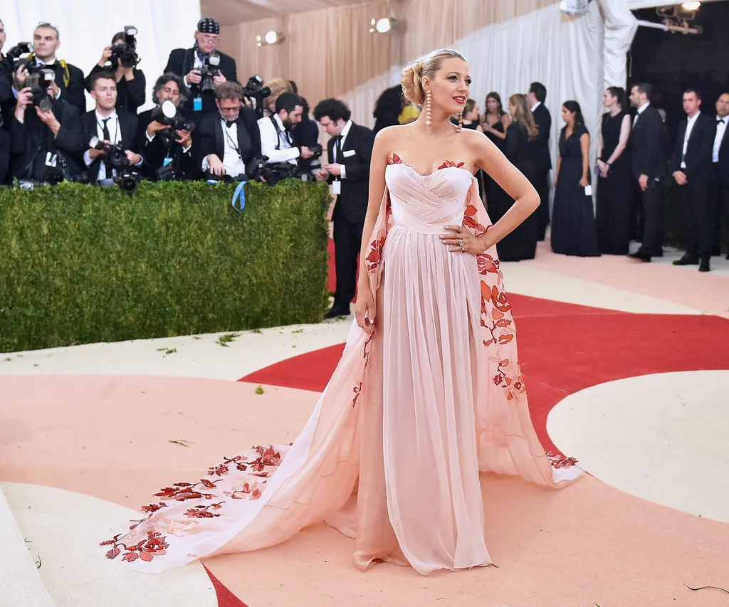 A blonde woman standing on a red carpet wearing a pink gown