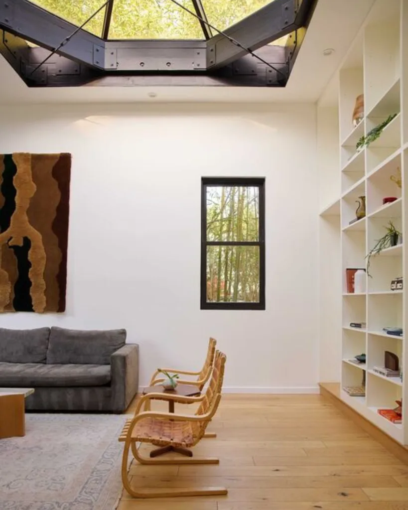 A living room with two timber chairs, grey couch, bookshelf and window