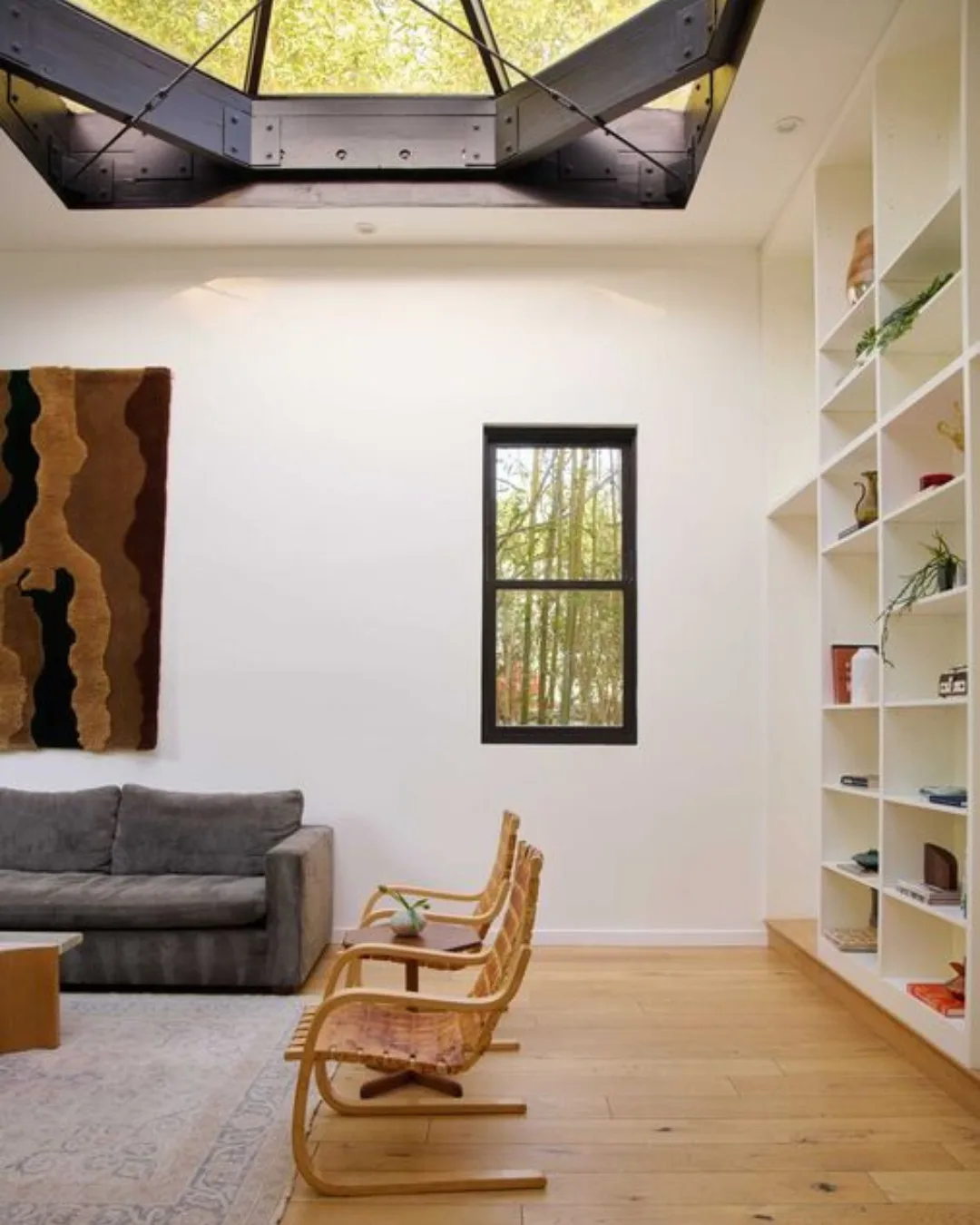 A living room with two timber chairs, grey couch, bookshelf and window 