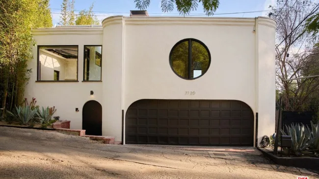 A white two-storey house with round windows and an arched black garage and front door