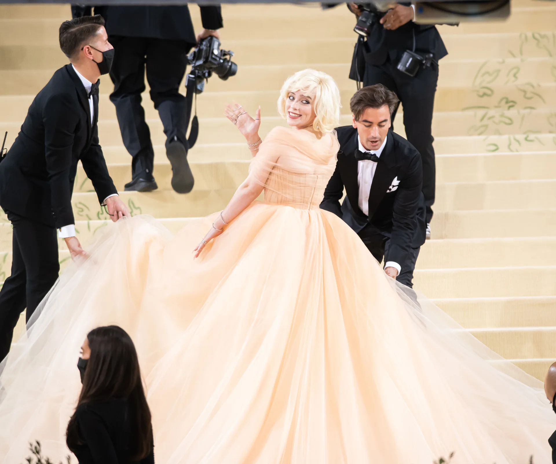 A woman wearing a peach gown surrounded by men wearing black suits