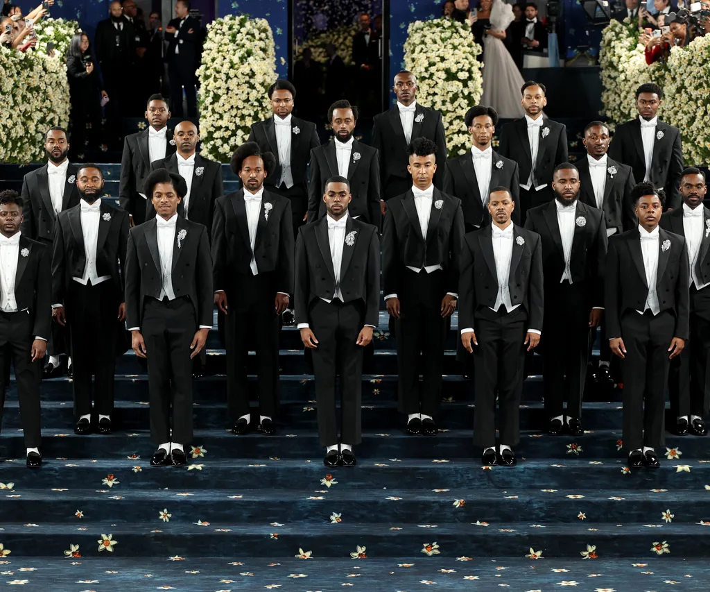 A group of men wearing black suits posing on a blue carpet