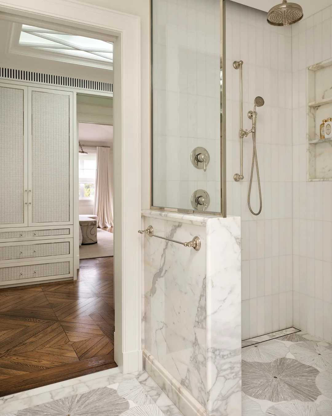 A white marble shower with metallic tapware, white kitkat titles and views into the walk-in-robe