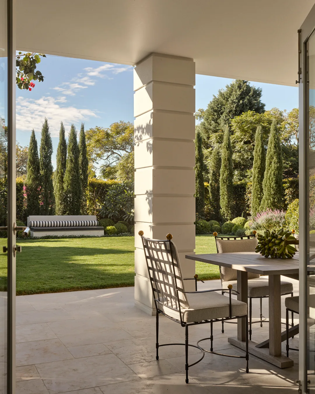 An outdoor area with greenery, dining table and, black and white striped day bed