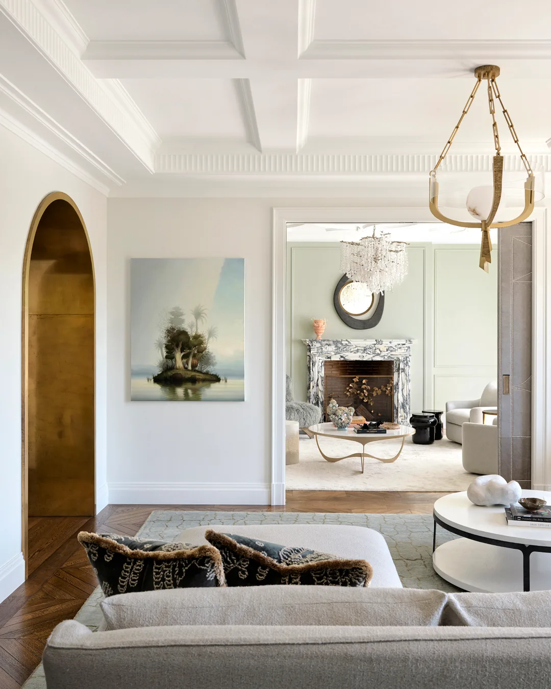 A view from living room to formal living room with grey couch, abstract rug, white coffee table and contemporary, gold chandelier