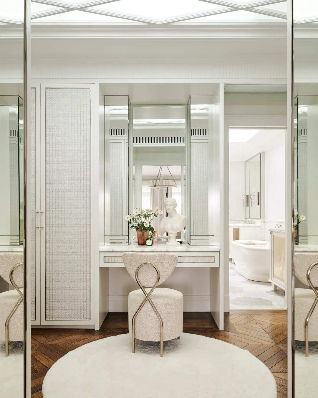 A walk-in-robe with mirror panelling, timber flooring, white stool and rattan doors