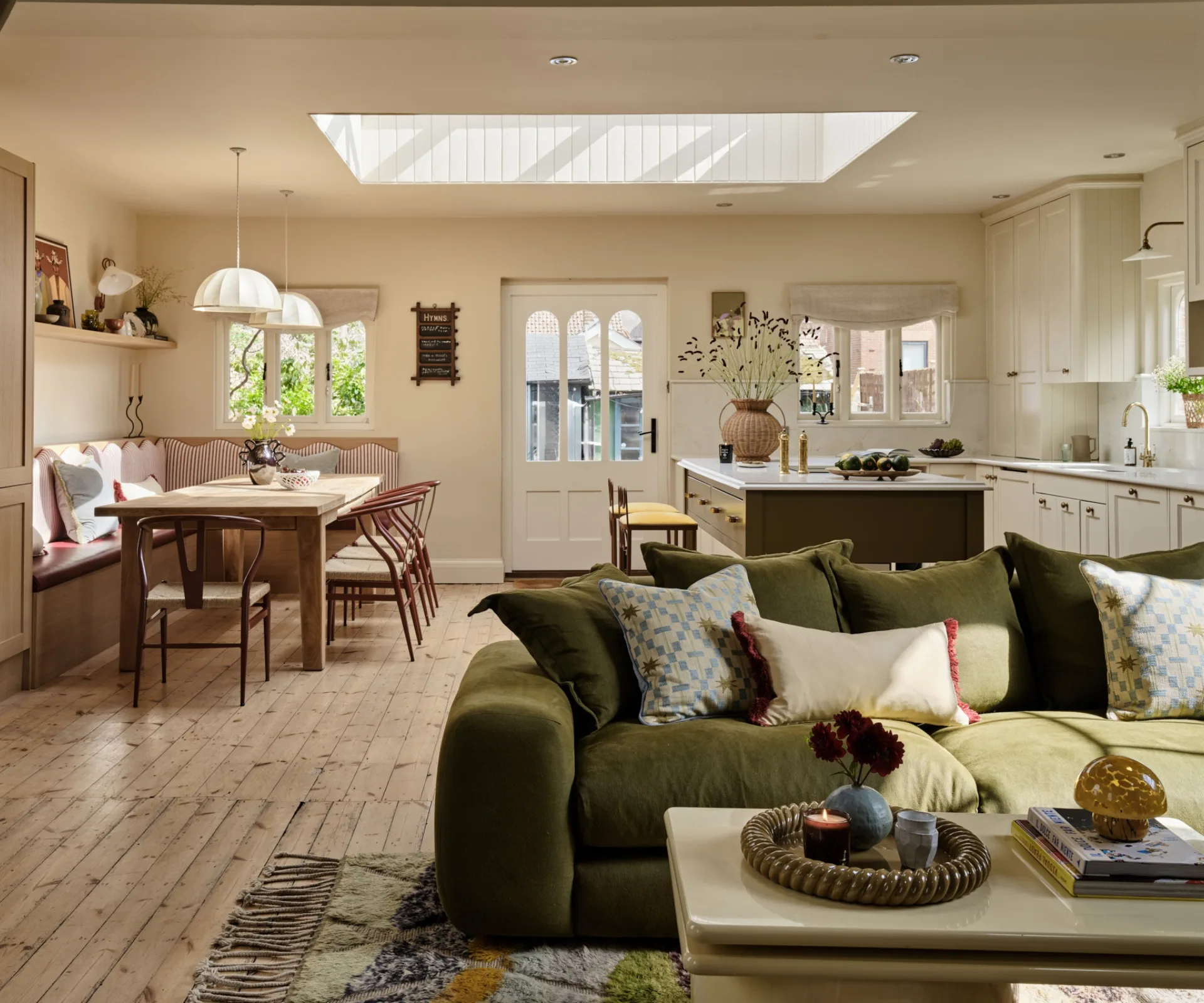 Open-plan living, kitchen and dining space in a converted chapel owned by SheerLuxe fashion director, Polly Sayer, with olive-green sofa, patterned cushions, oak floors, skylight and built-in banquette seating.