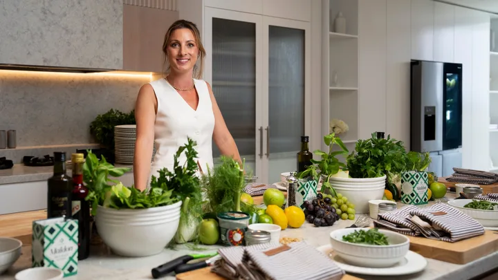 Author and chef Amanda Cordony standing in a kitchen with fresh green produce on the benchtop.
