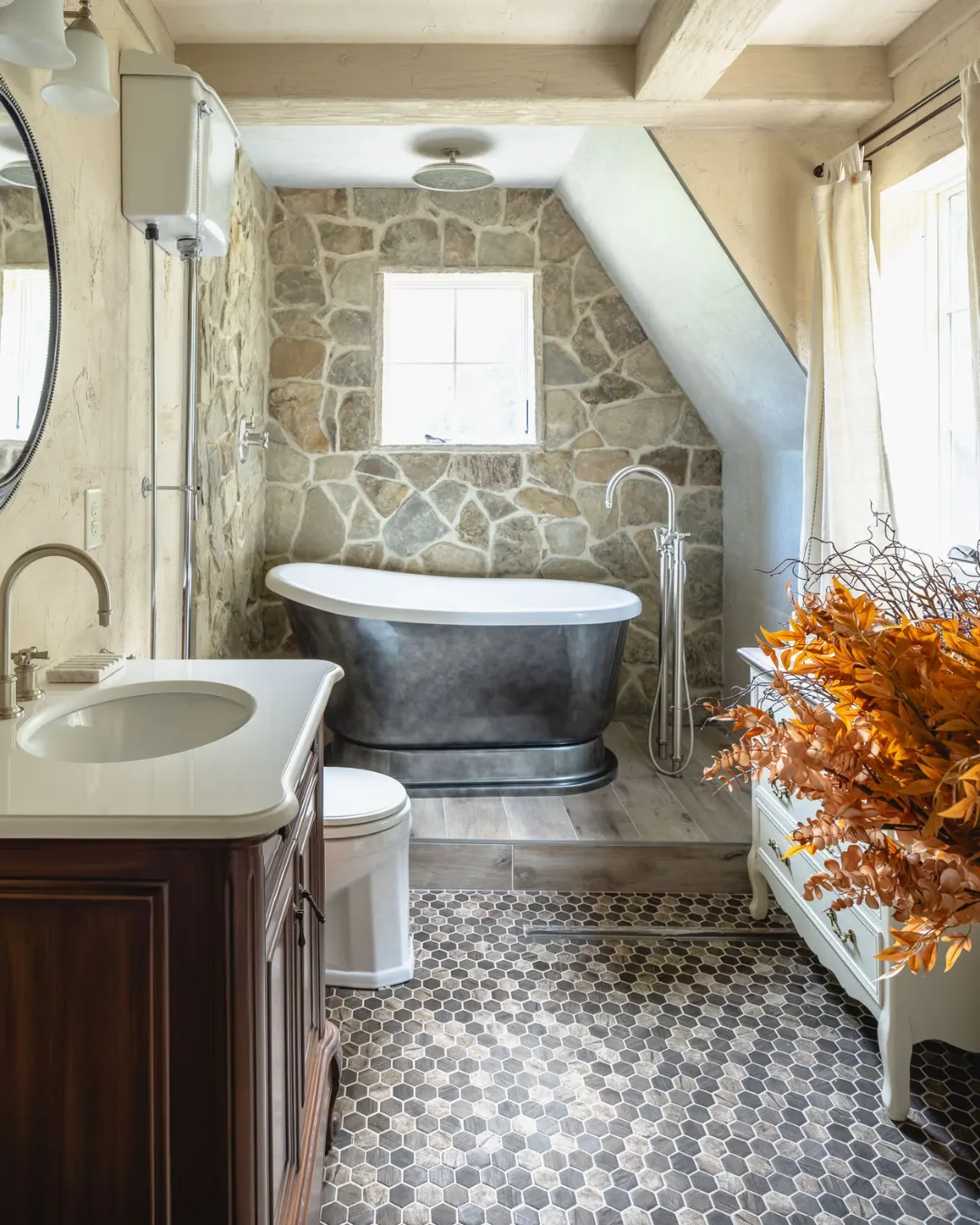 A bathroom with silver bathtub, stone walls, and pattern tiles.