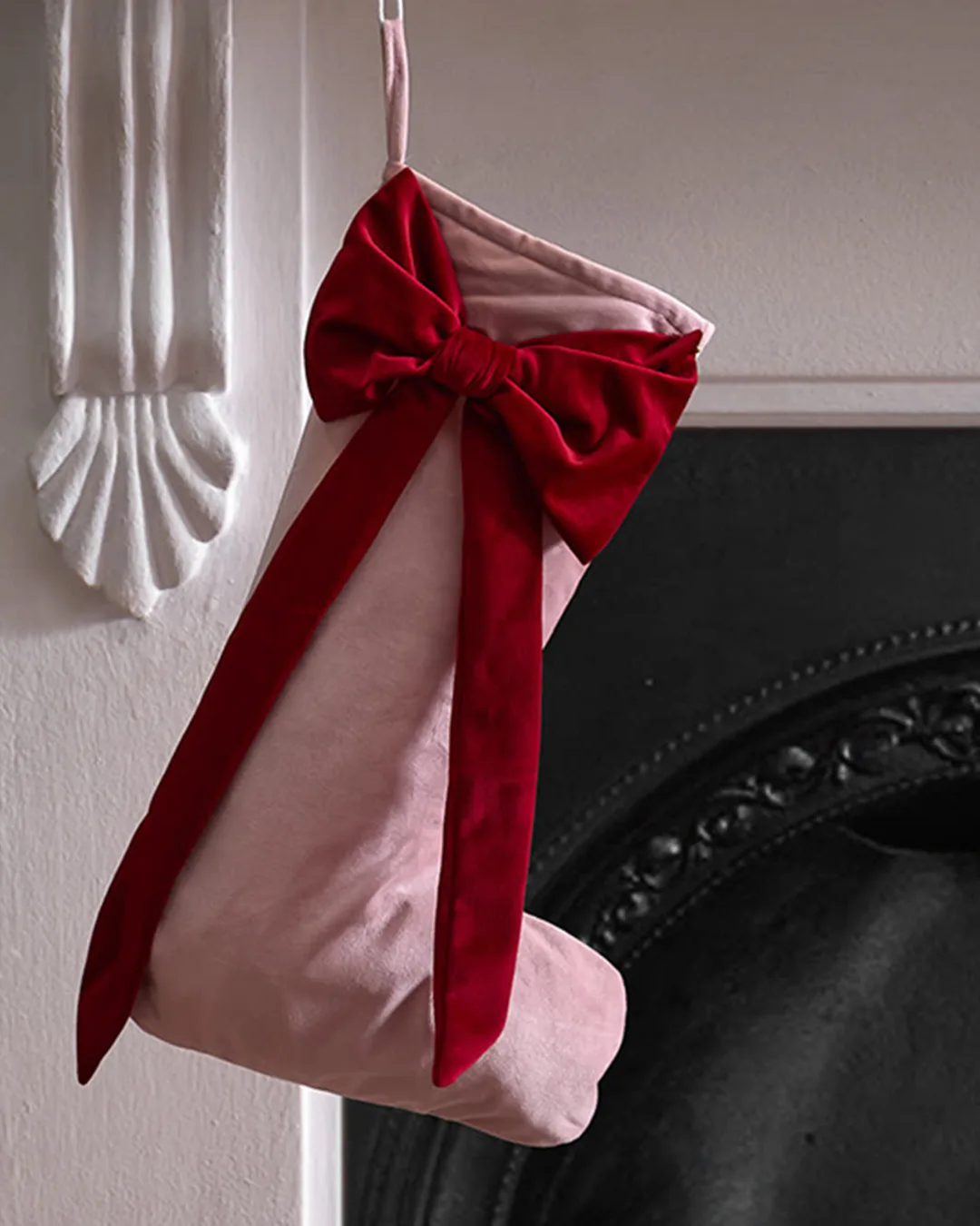 A pink Christmas stocking with a red bow hanging from a fireplace with white walls