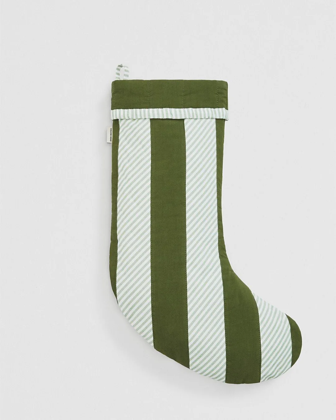 A green and white stripe traditional Christmas stocking with a loop against a grey background