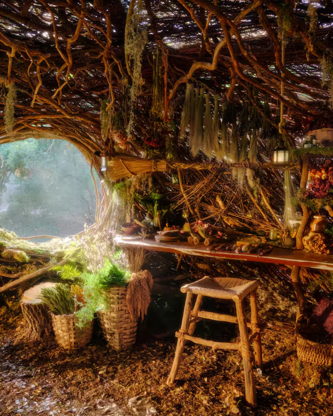 A timber desk, with a broom hanging on the wall made of roots and baskets filled with greenery