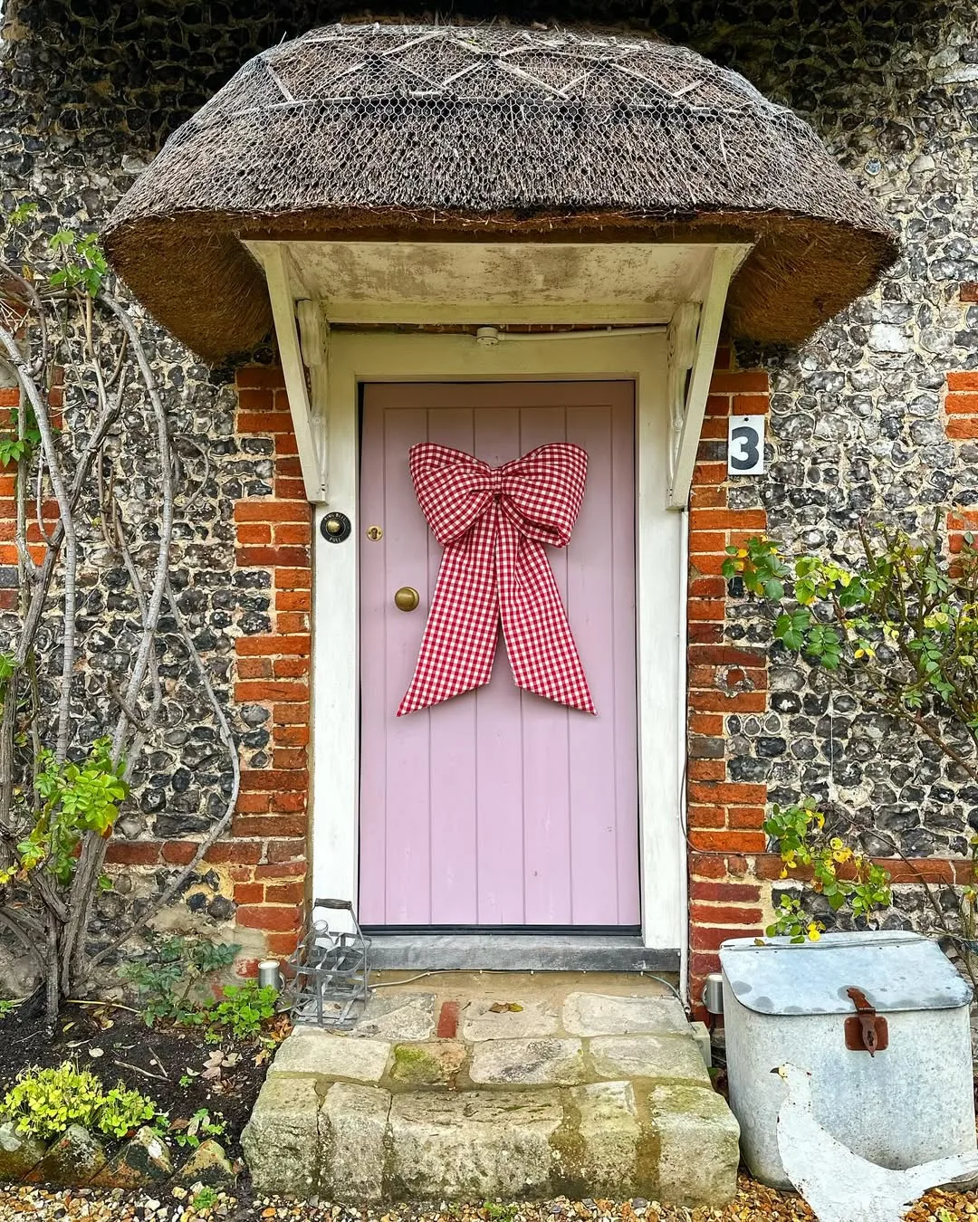A brick house with a pink door and a big red and white gingham bow on the door 