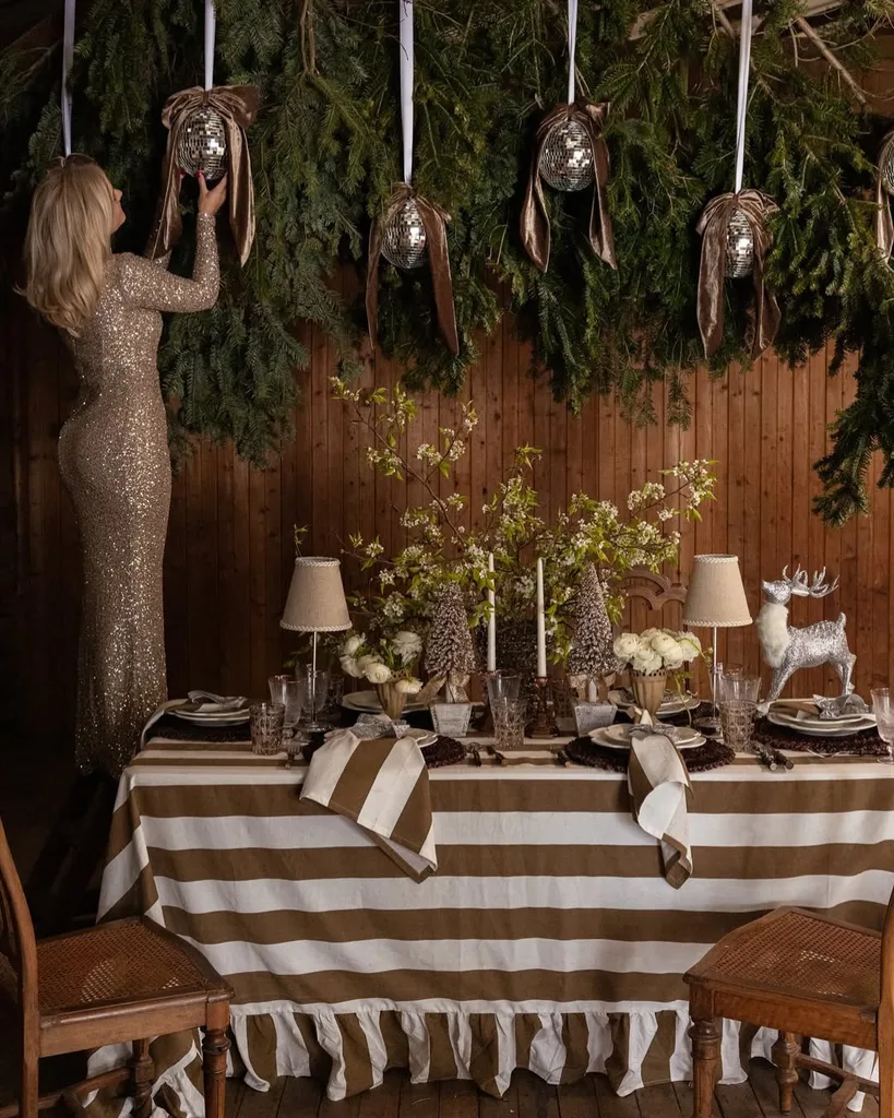 A woman standing on a chair fixing decorations next to a table with a beige and white stripe tablecloth
