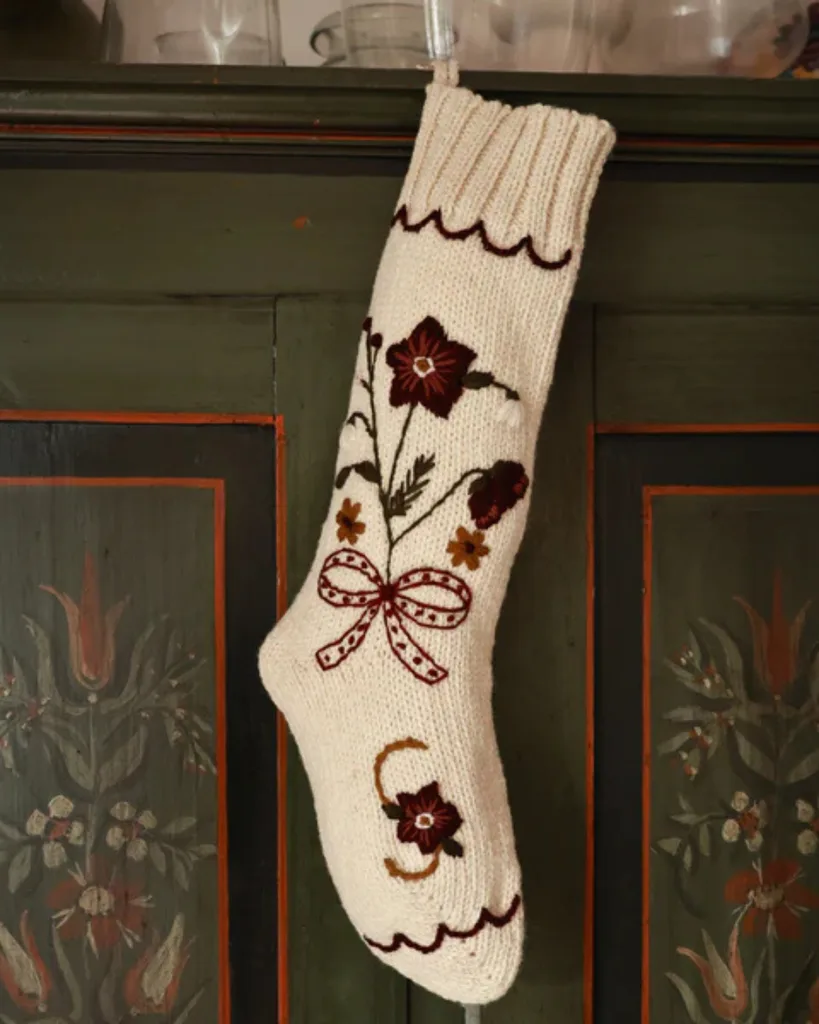 A white wool embroidered stocking hangs on a green wall decorated with paint