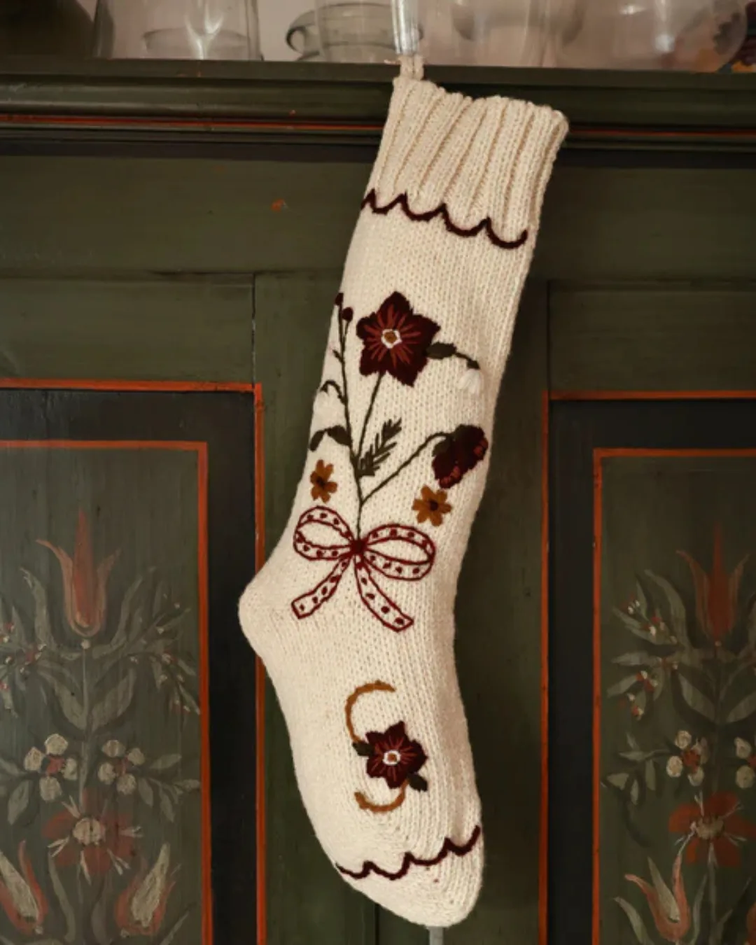 A white wool embroidered stocking hangs on a green wall decorated with paint