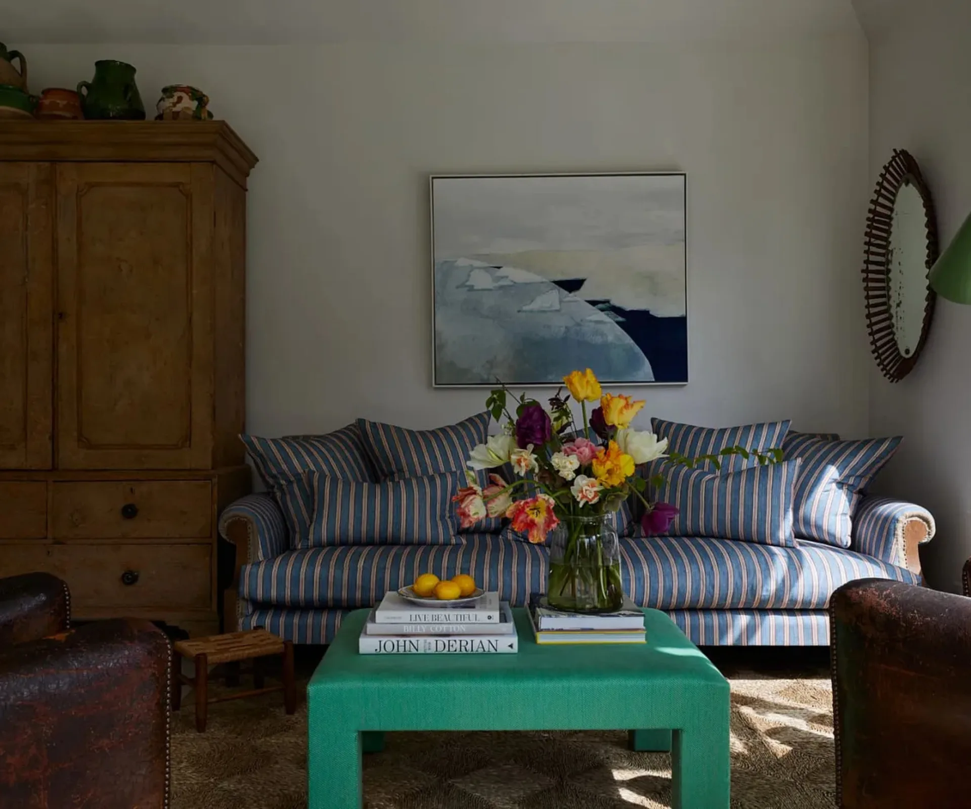 A blue and white stripped couch, a green coffee table, a timber vintage cabinet and artwork