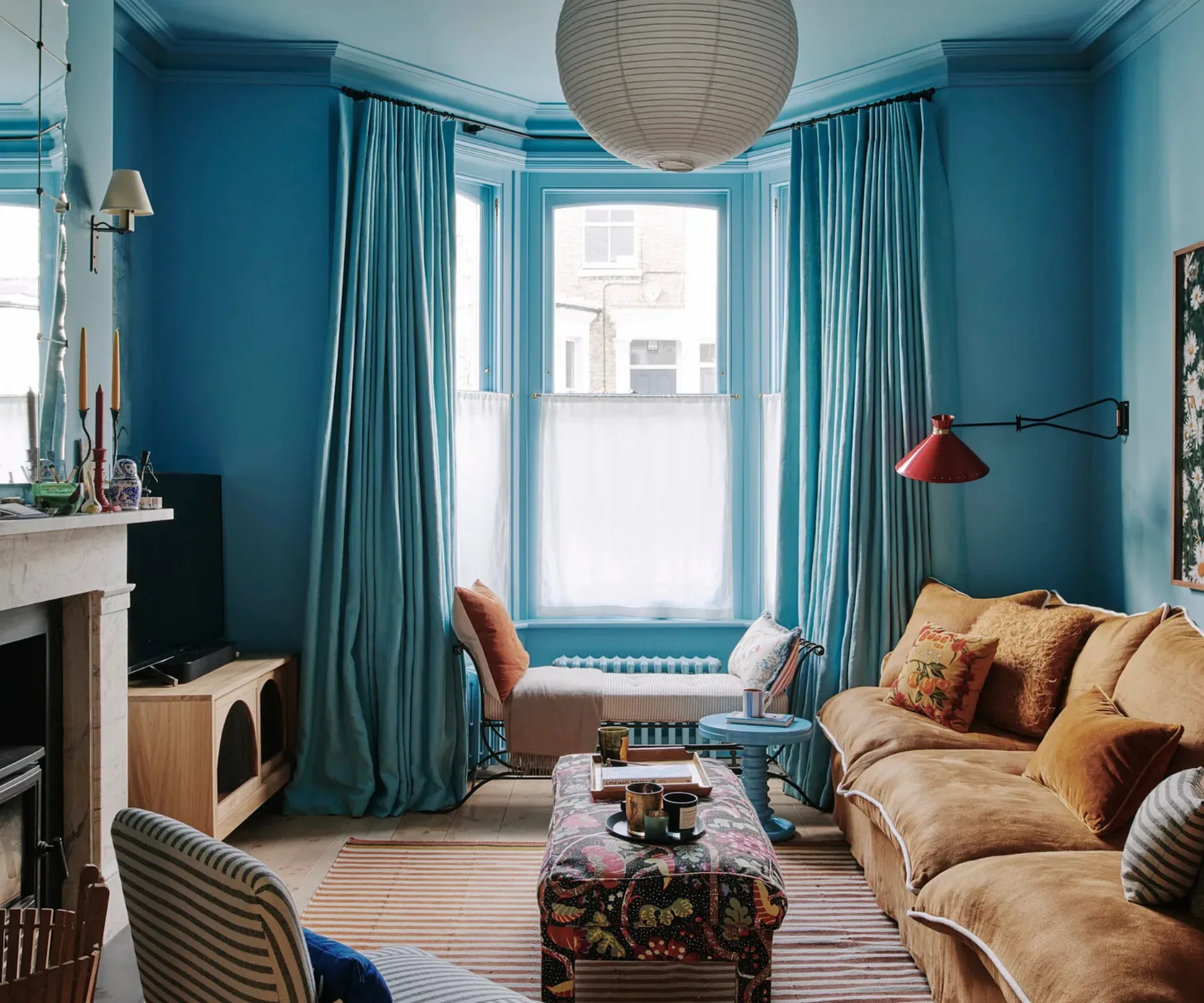 A blue living room with brown sofa, paper lantern, pattern coffee table and striped chair