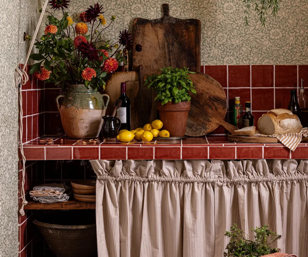 A corner of kitchen island with wood cutting board, flowers, lemons, and herbs in clay pot