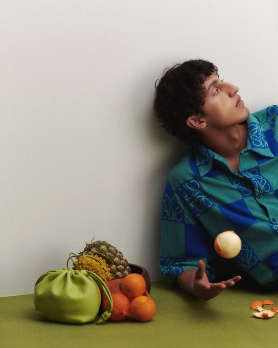 Loewe campaign with man in blue shirt, a green bag, oranges and papaya sitting on the floor 