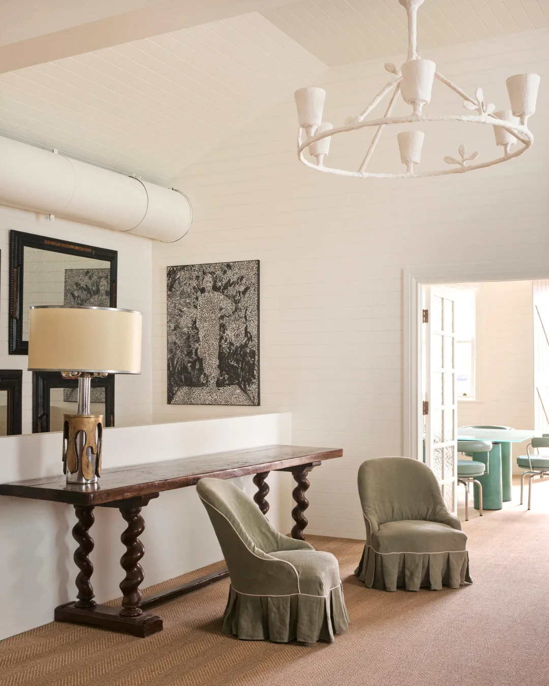 Two khaki linen armchairs, timber table, abstract art, white chandelier, and mirror 