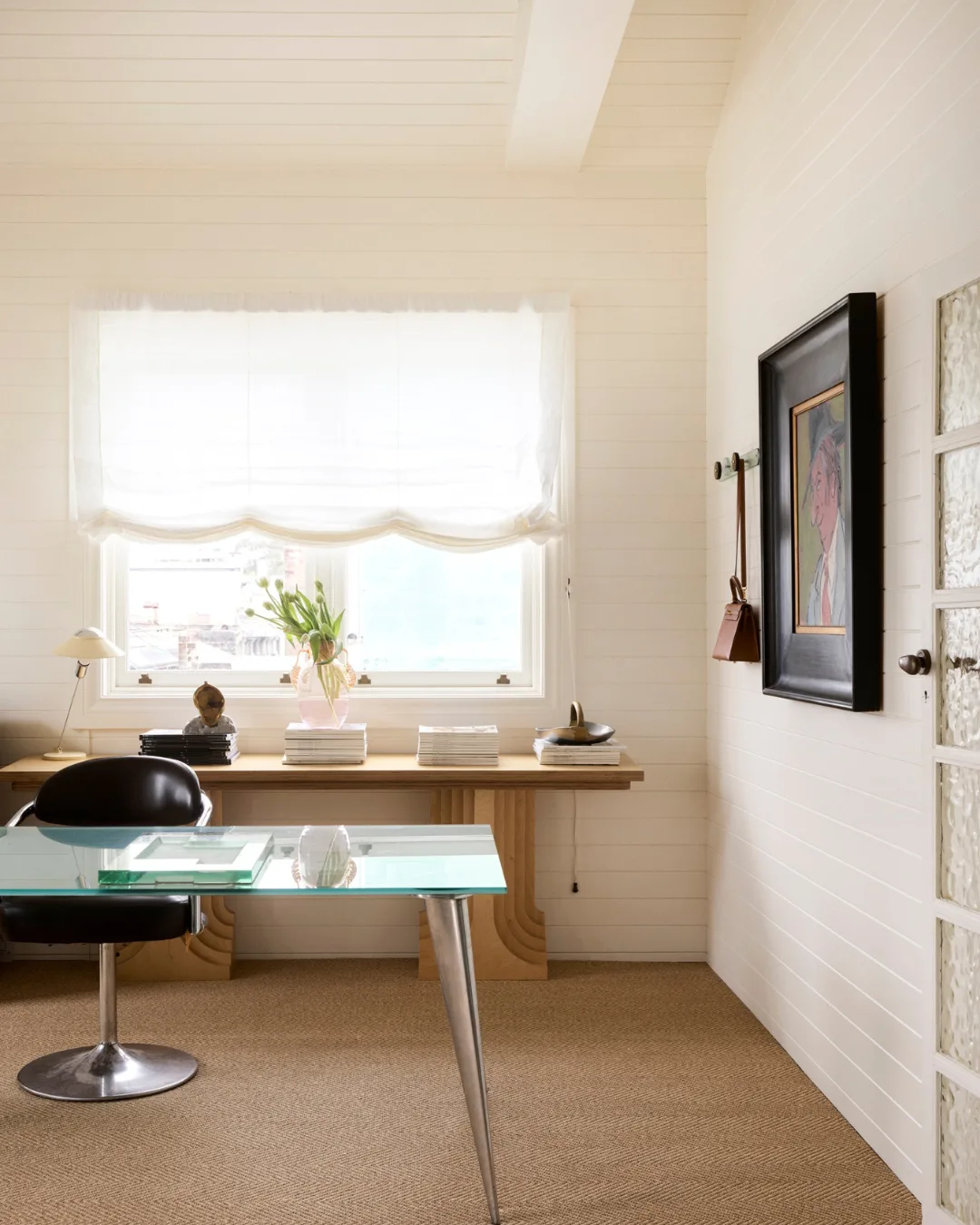 A glass desk, black leather chair and historic artwork 