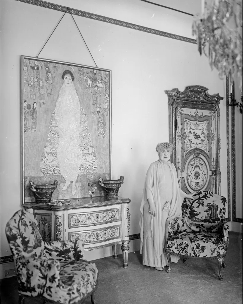 Black and white photo of a woman in sideboard, two pattern armchairs and an artwork of a woman hanging on the wall