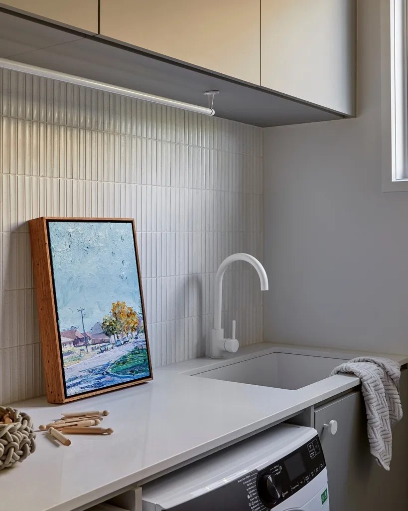 A landscape painting sits on the laundry bench against a tiled backsplash.