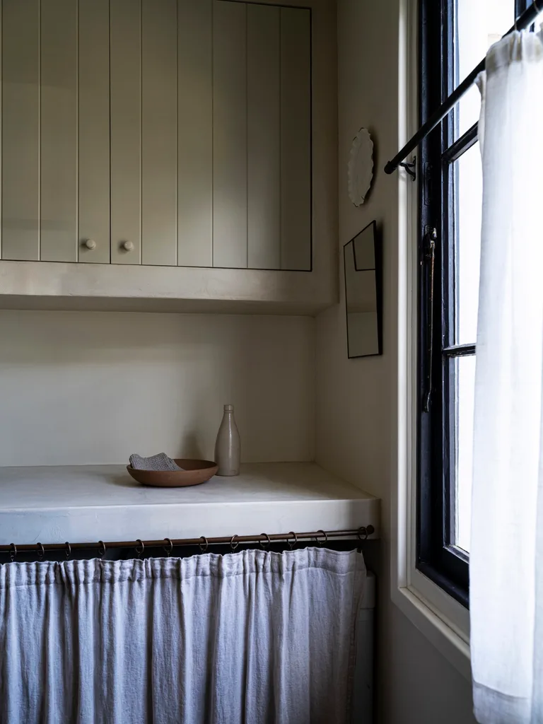 A rustic laundry featuring a microcement bench top and linen curtains