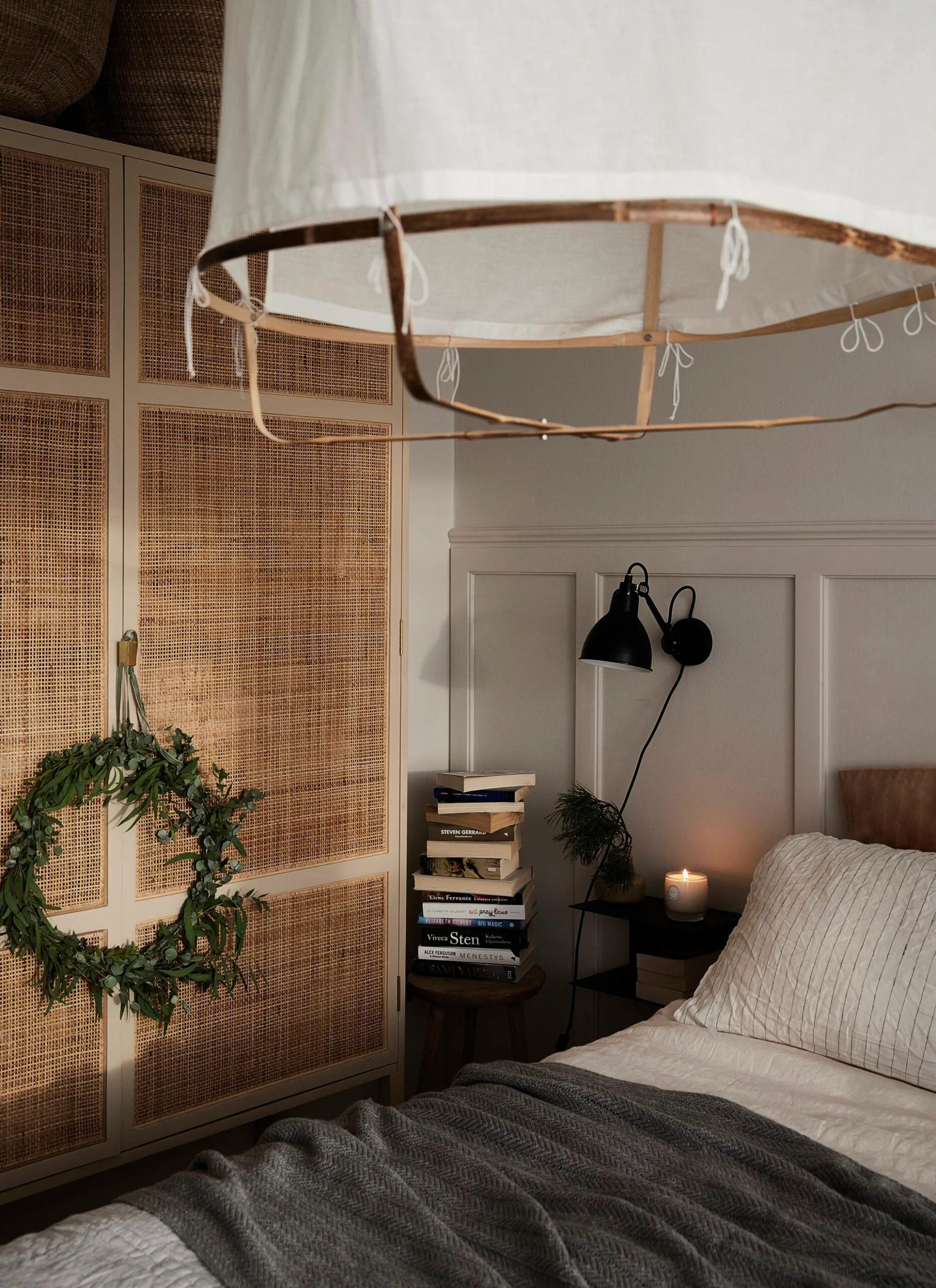 A Scandi bedroom with white bedding and a bedside table stacked with books