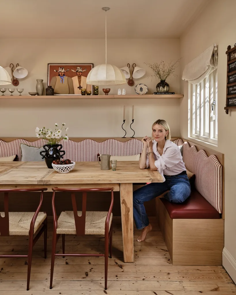 Fashion director Polly Sayer sits in her dining nook with striped banquette, oak table and wall shelf of ceramics - timeless English country kitchen inspiration.