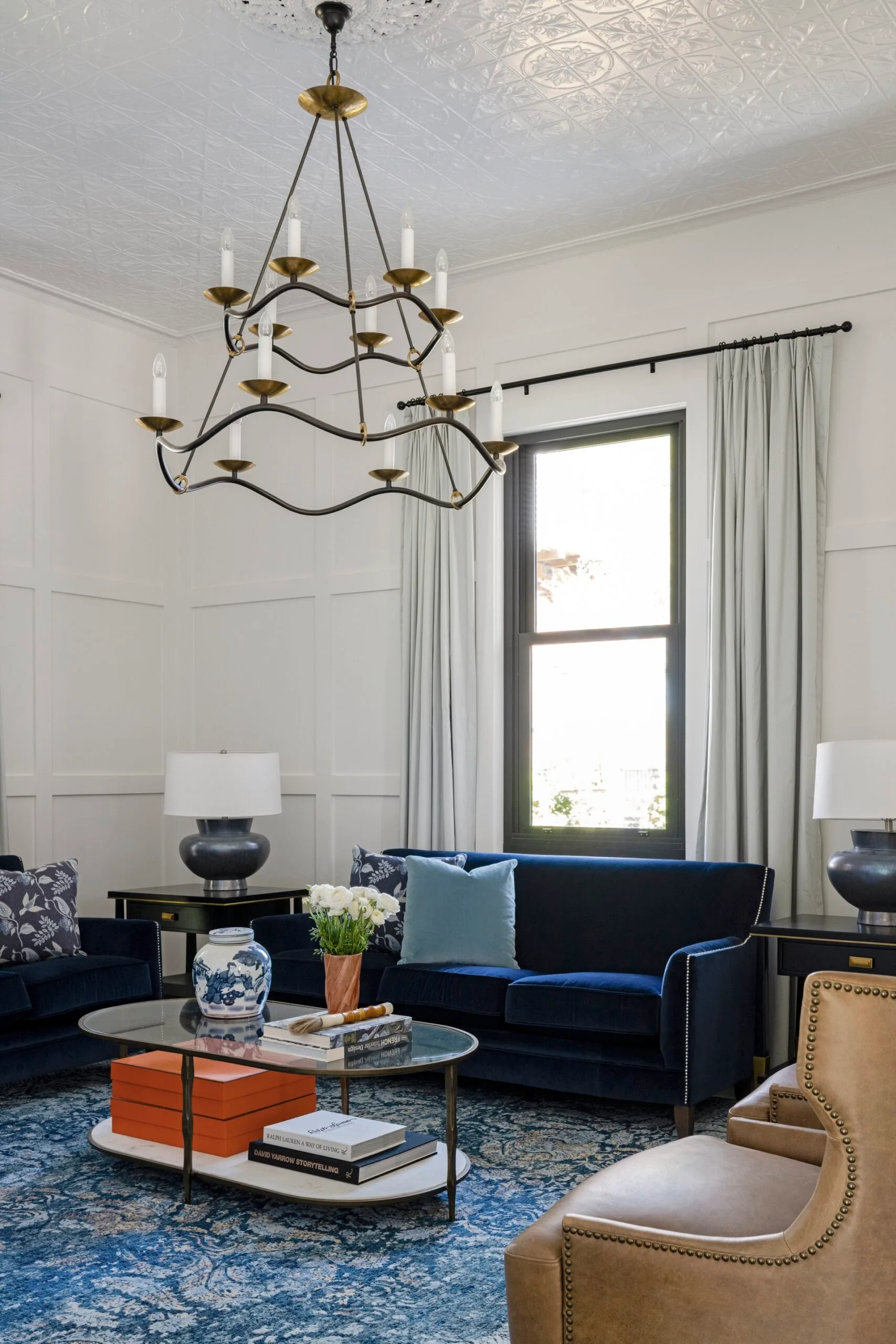 A formal lounge with a blue velvet sofa and modern chandelier