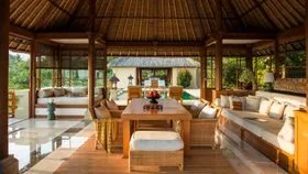 A tropical pergola with white cushions, rattan furniture and a pool at a luxury bali villas