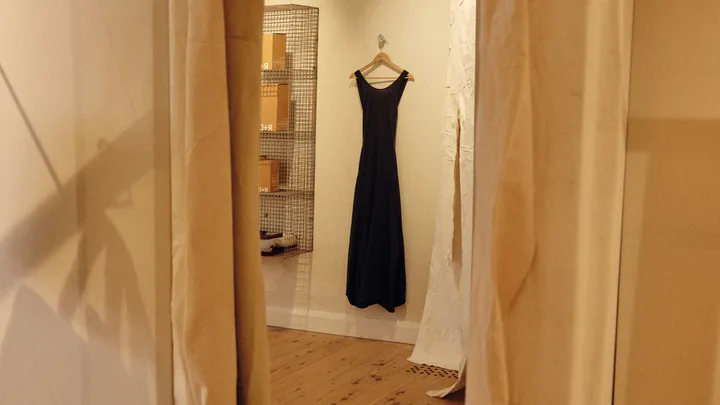 A black midi dress hanging on a cream wall, seen in reflection of mirror.