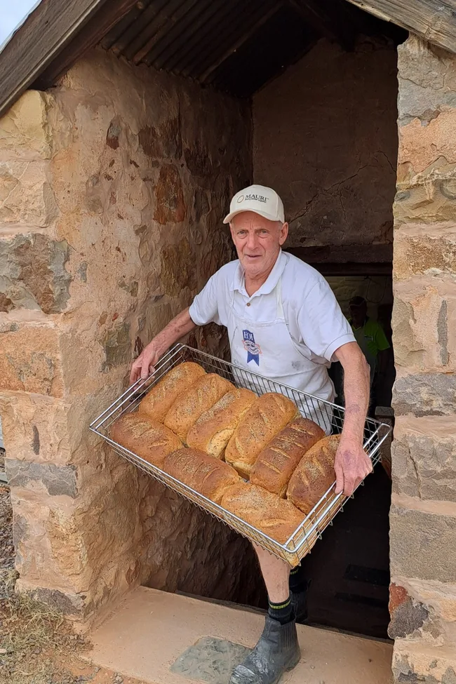 A baker holding a tray of bread loaves at Farina Bakery