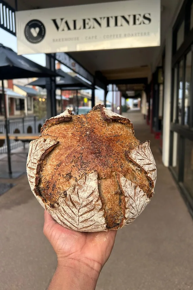 A person holding a fresh loaf of bread outside Valentine's Bakery