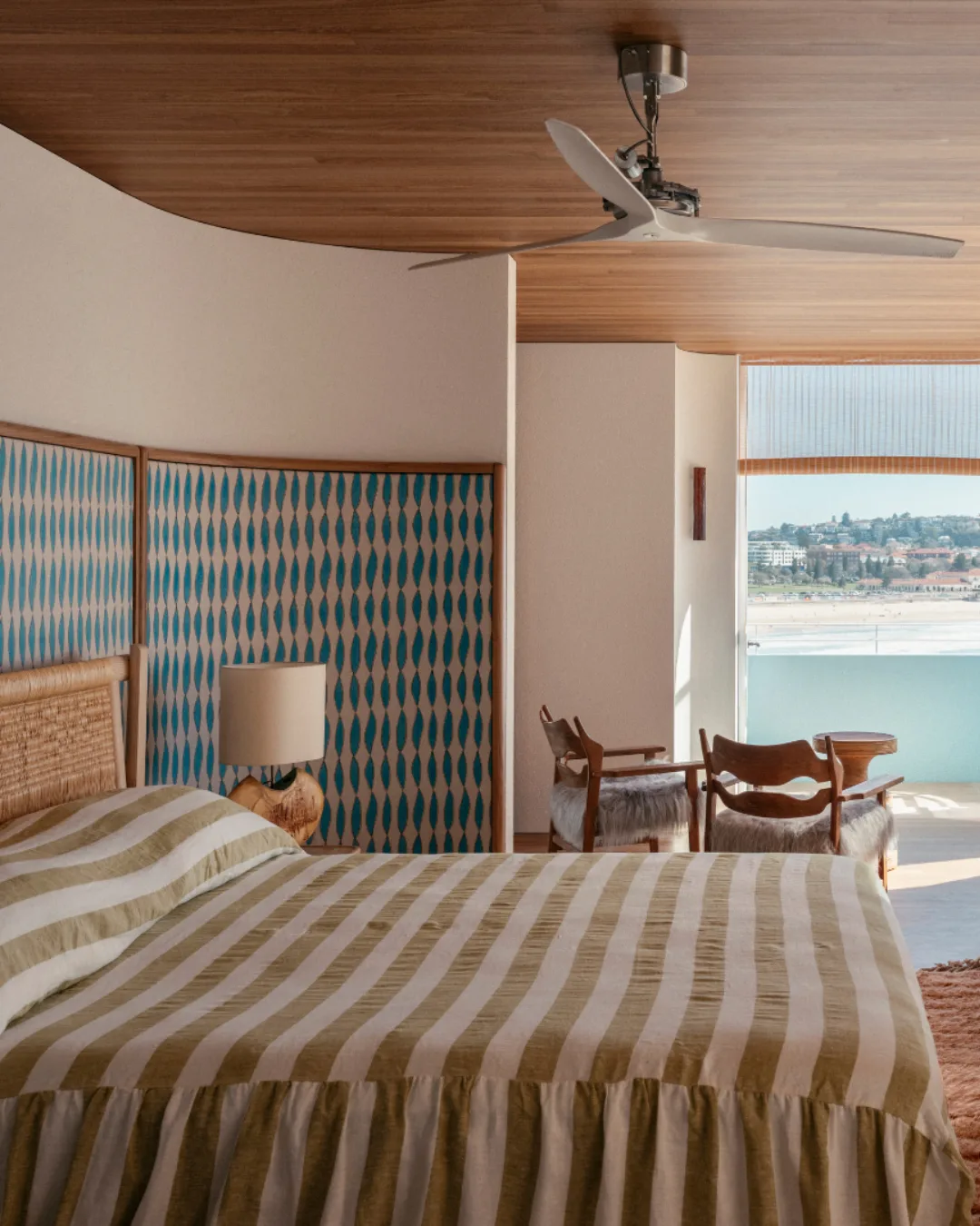 Modern bedroom with striped bedding, natural wood accents, beach-themed decor, ocean view.